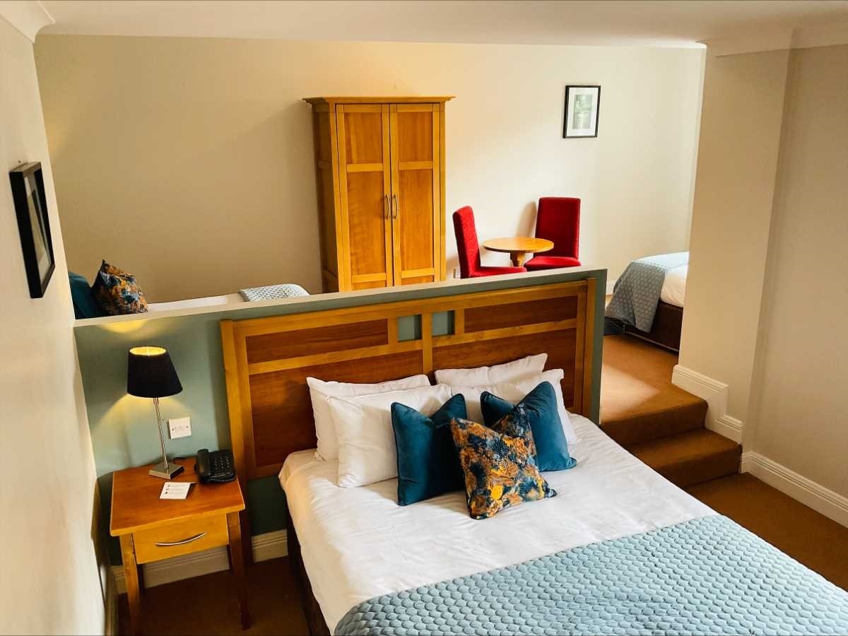 Hotel room with a bed, wooden furniture, and red chairs.