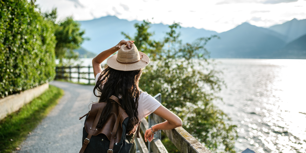 Person with hat and backpack overlooking a lake and mountains.