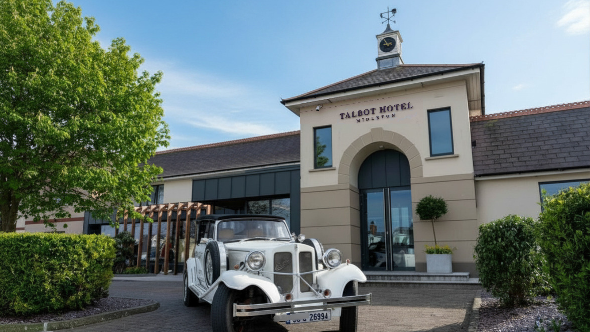 A white vintage car parked in the driveway in front of the Talbot Hotel Midleton entrance.