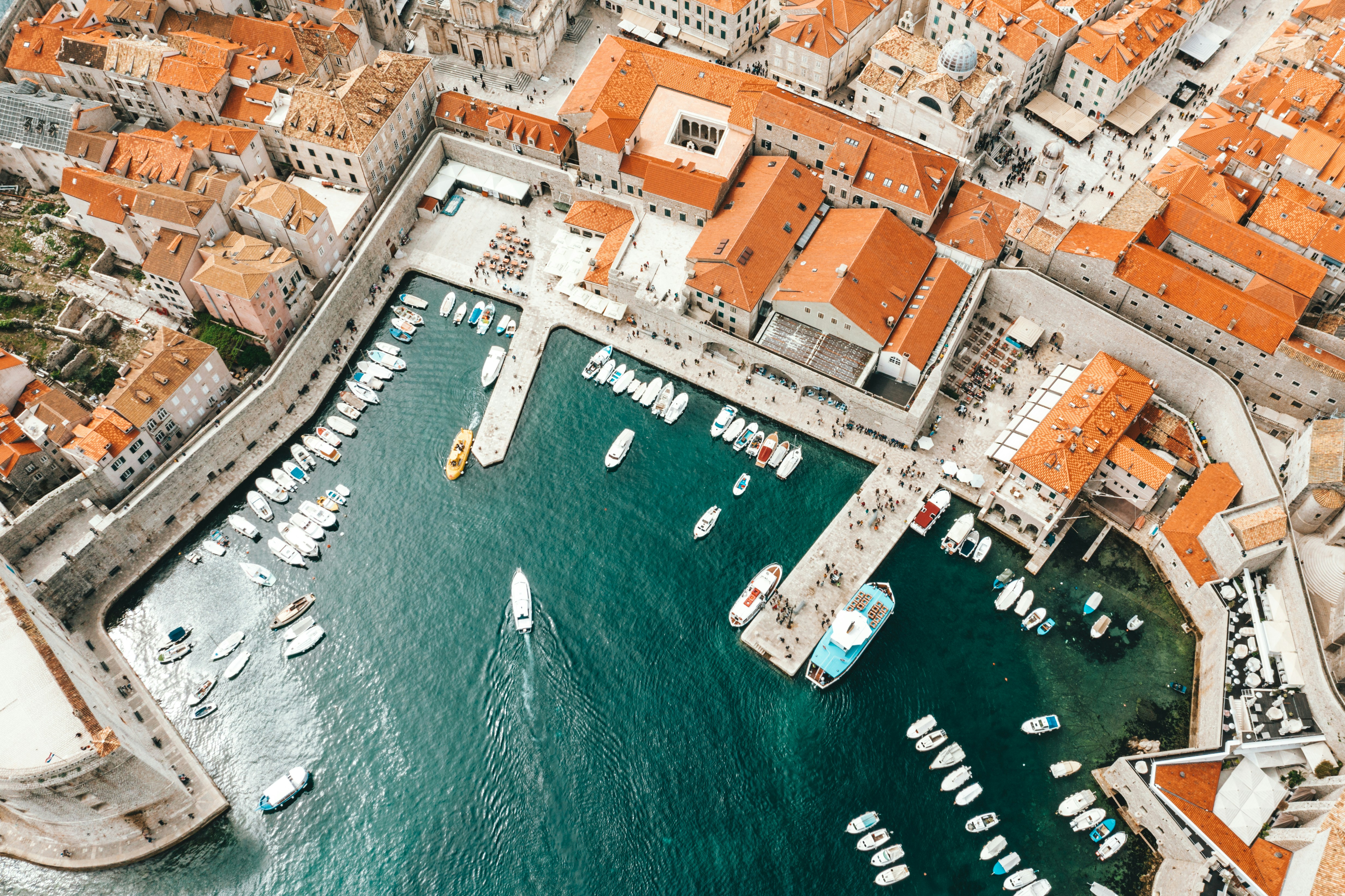 Aerial view of a harbor with boats and orange-roofed buildings.