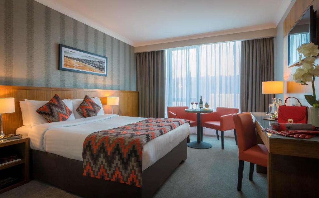 A hotel room with a made bed, a seating area with a small table, and a desk.