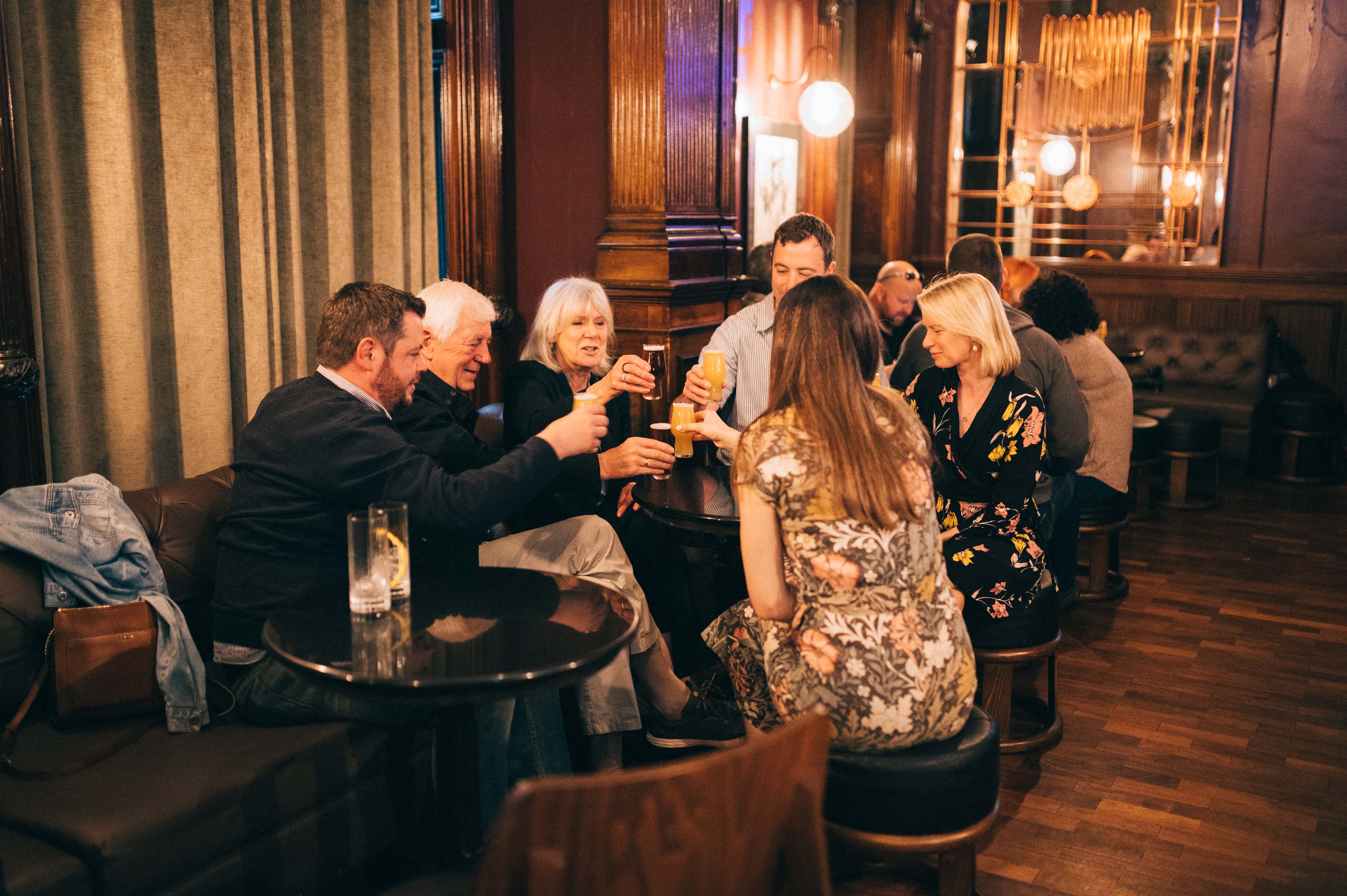 A group of people sitting around a table in a dimly lit bar, toasting with their drinks.