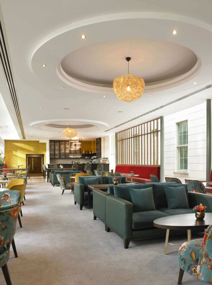 Modern lounge with colorful seating, round tables, and decorative ceiling lights.