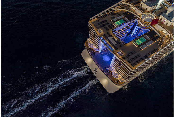 Aerial view of a cruise ship with illuminated decks at night.