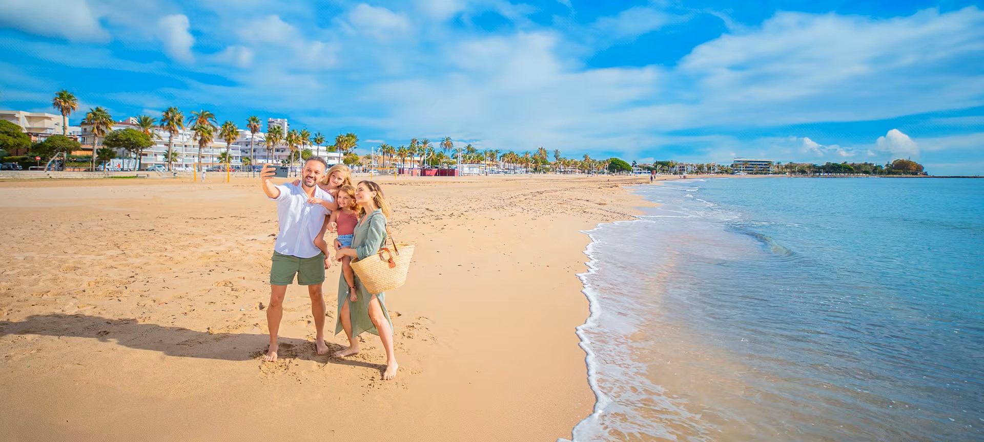 Family taking a selfie on a sunny beach with palm trees.