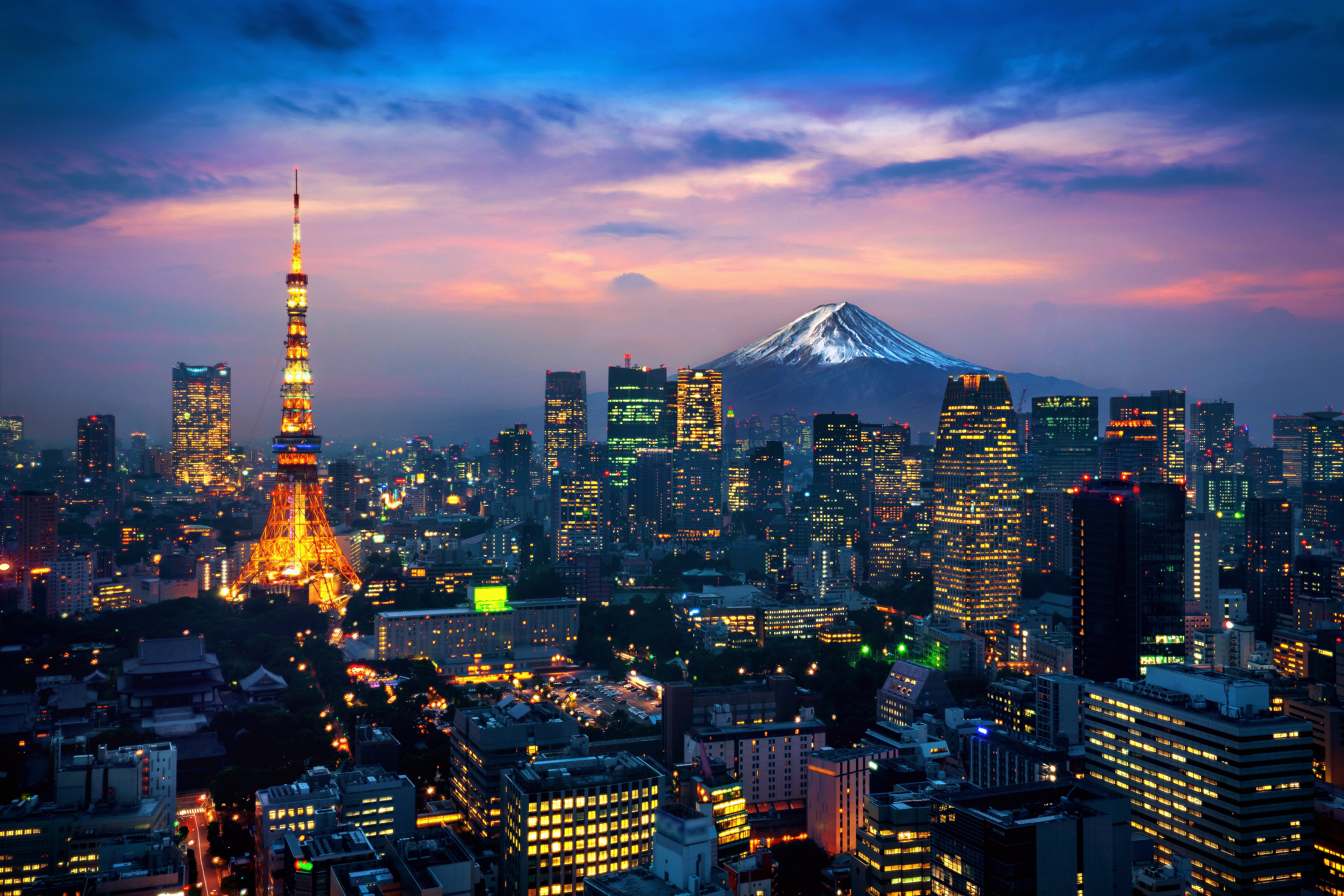 City skyline at dusk with a lit tower and mountain in the background.