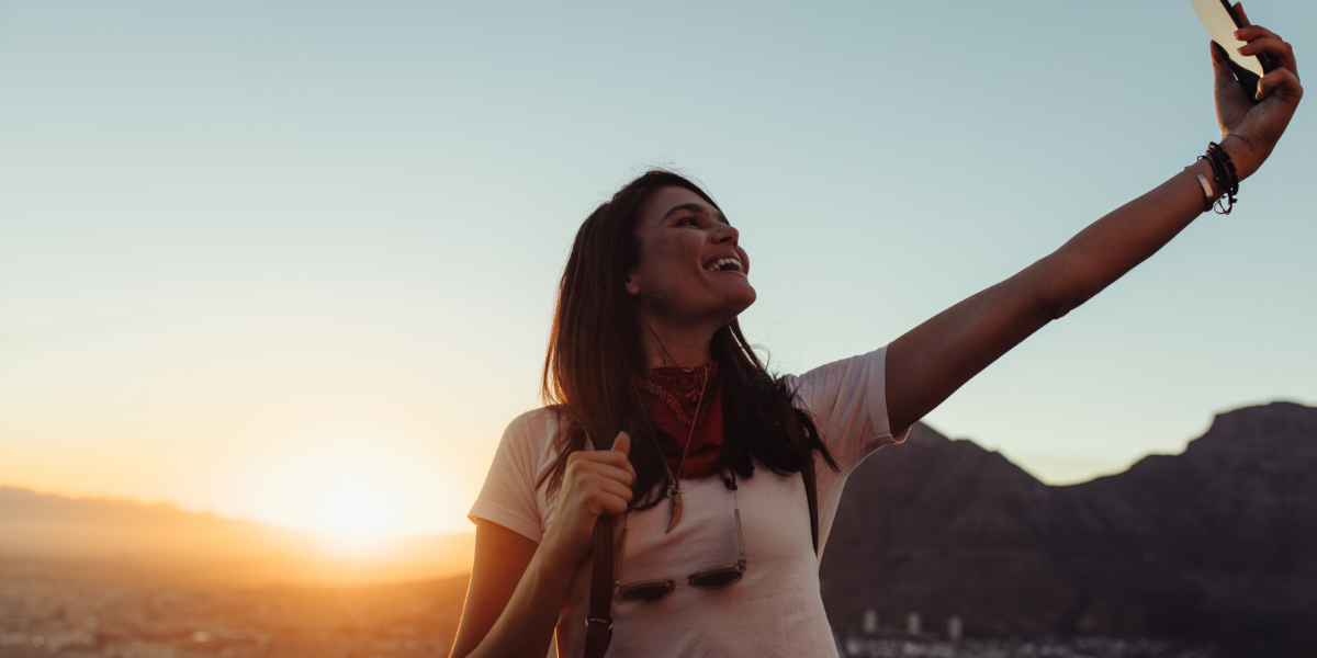 Person taking a selfie at sunset with mountains in the background.