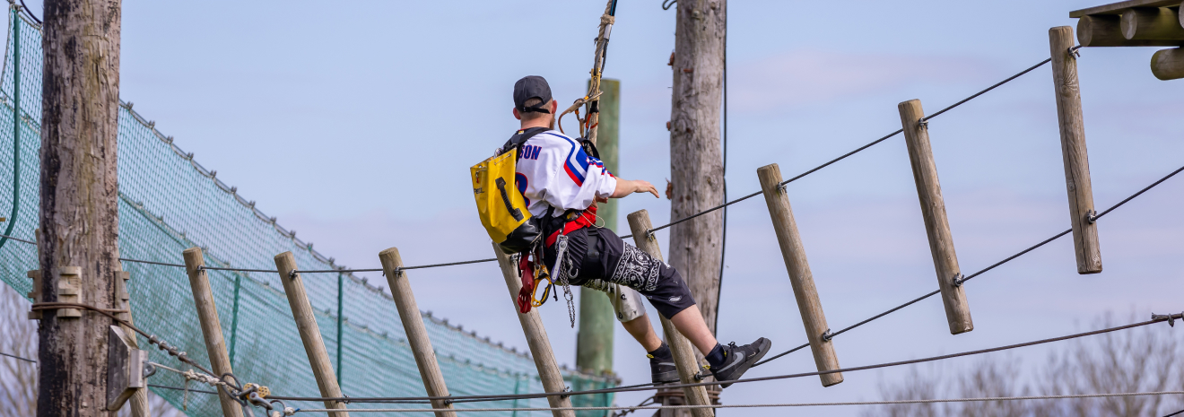 Person navigating a high ropes course with safety harness.
