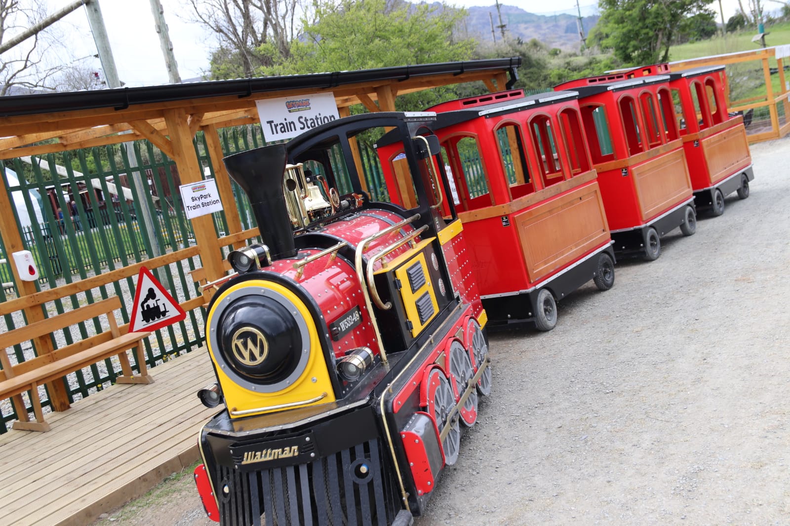 Miniature red train at a small outdoor train station.