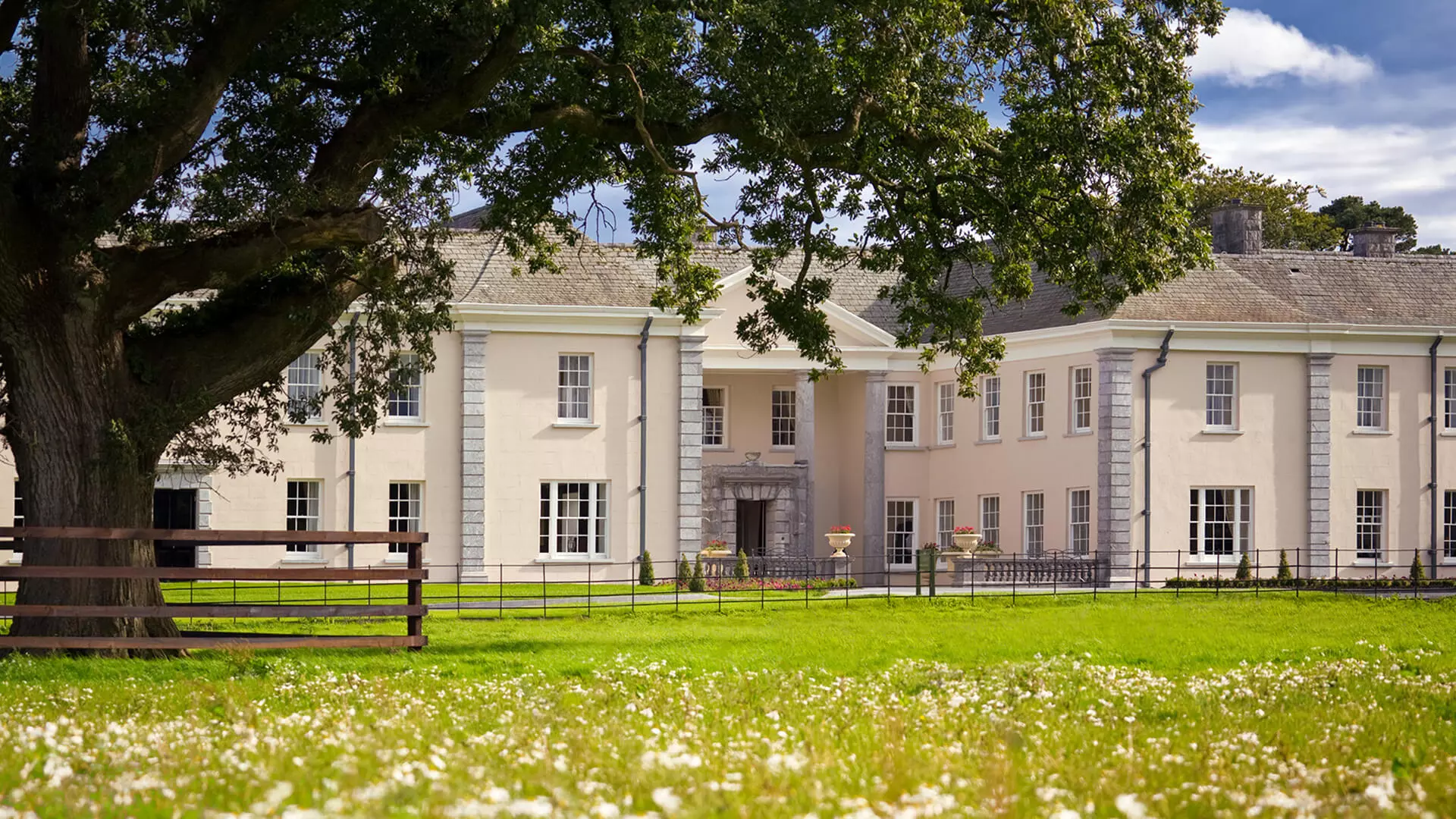 Large white mansion with columns, surrounded by green lawn and trees.