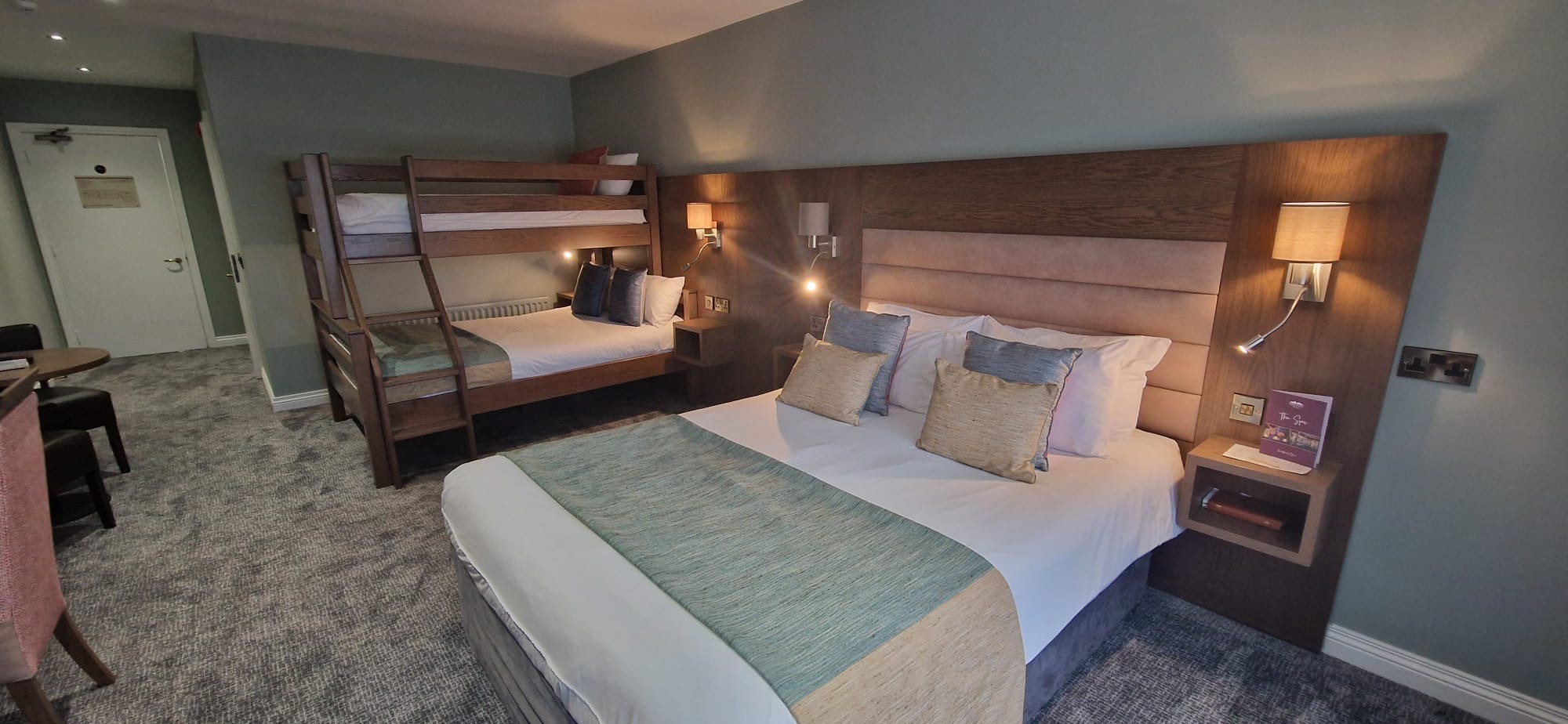 A modern hotel room featuring a large double bed and a wooden bunk bed in the corner.
