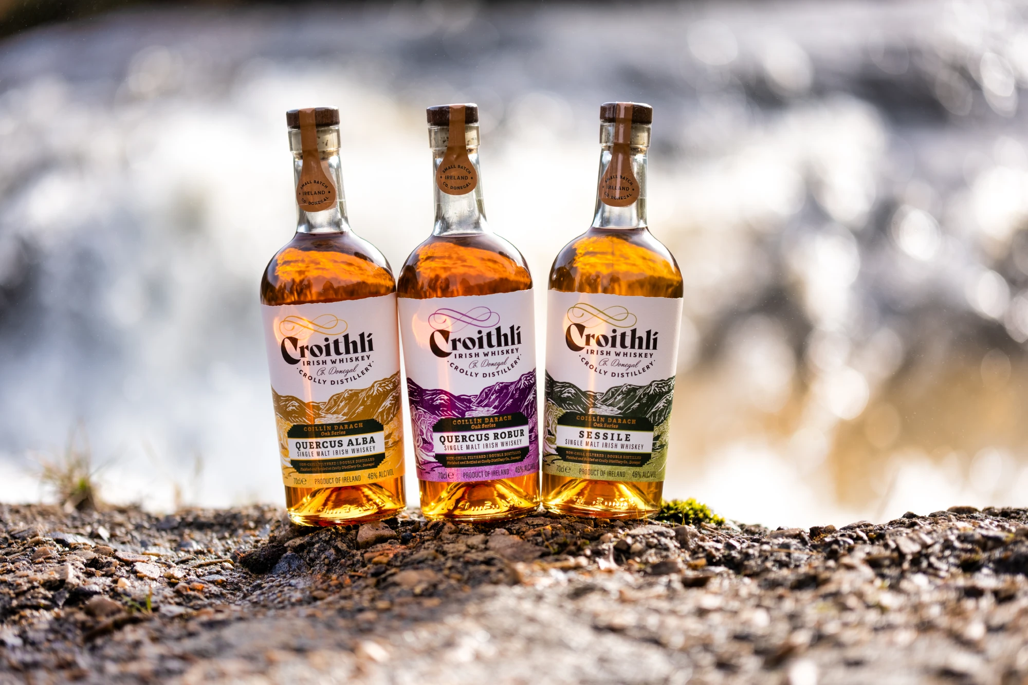 Three bottles of Croithlí Irish whiskey on a rocky surface with blurred background.