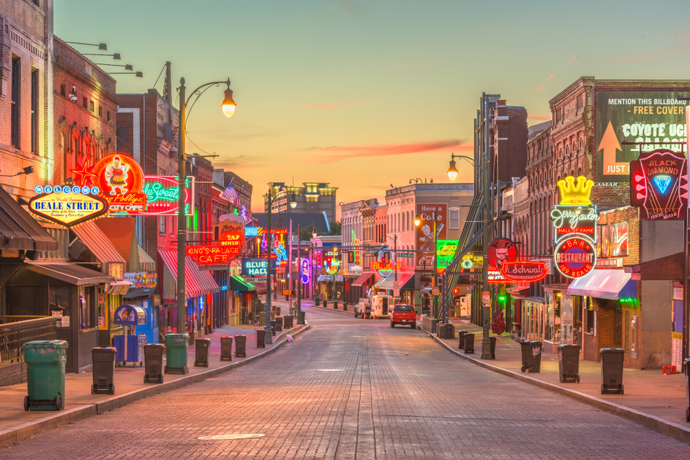 An empty Beale Street at dusk, with the cobblestones and neon signs illuminated by the setting sun.