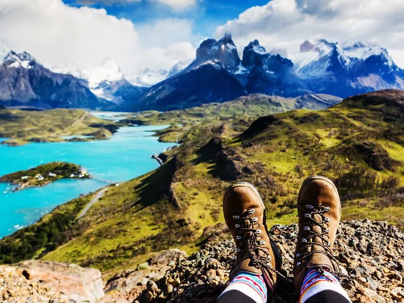 Person's feet in hiking boots overlooking a scenic mountain and lake view.
