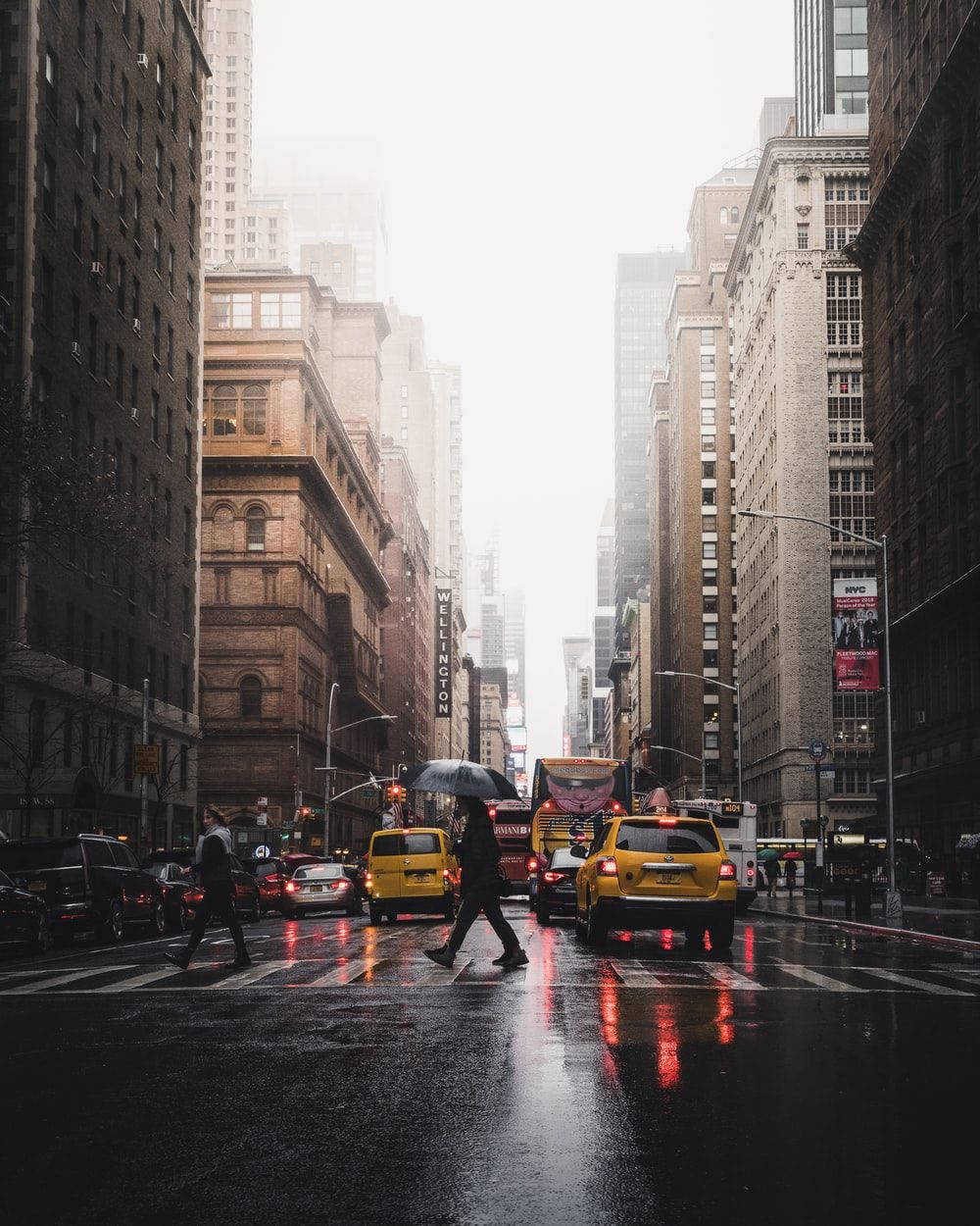Rainy city street with yellow taxis and a person crossing with an umbrella.