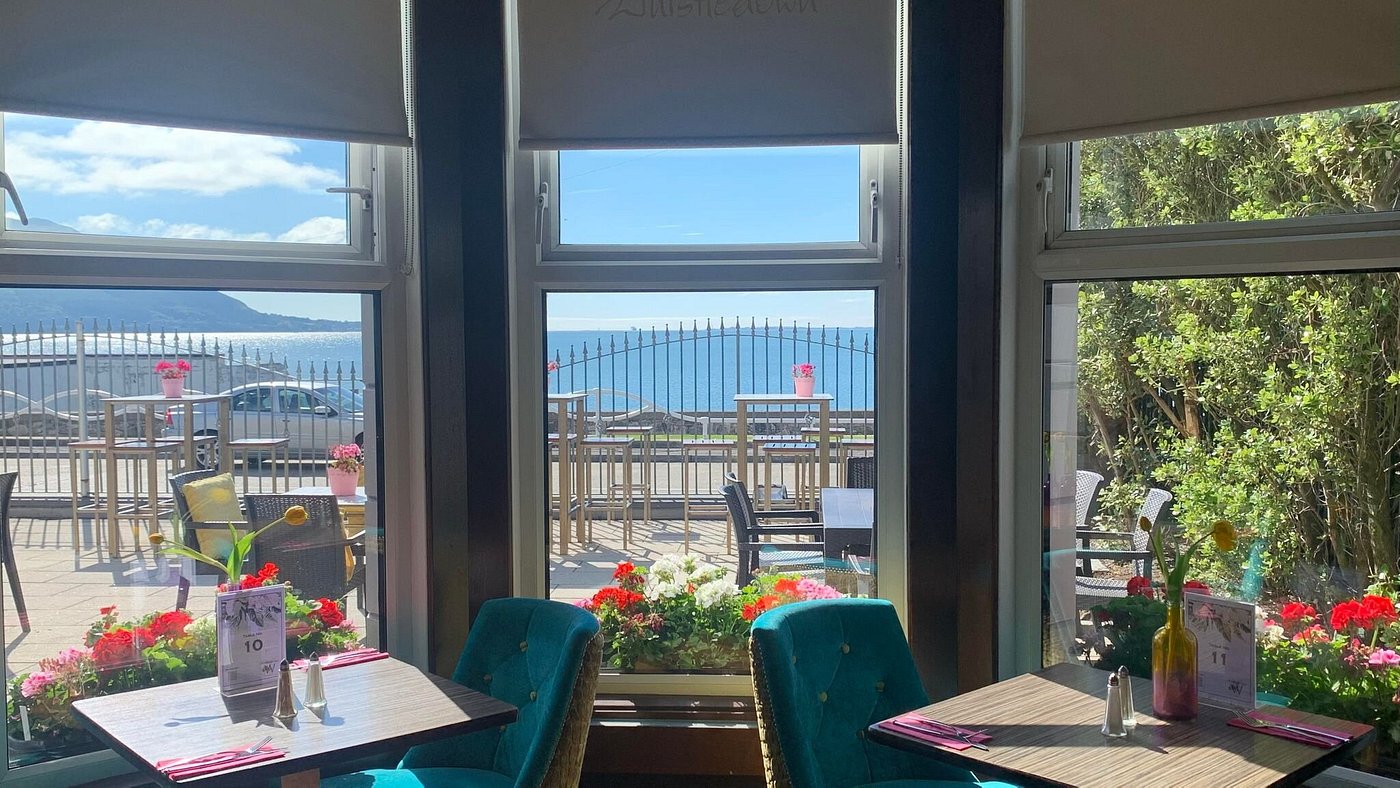 Cafe interior with tables, chairs, and a view of the sea through large windows.