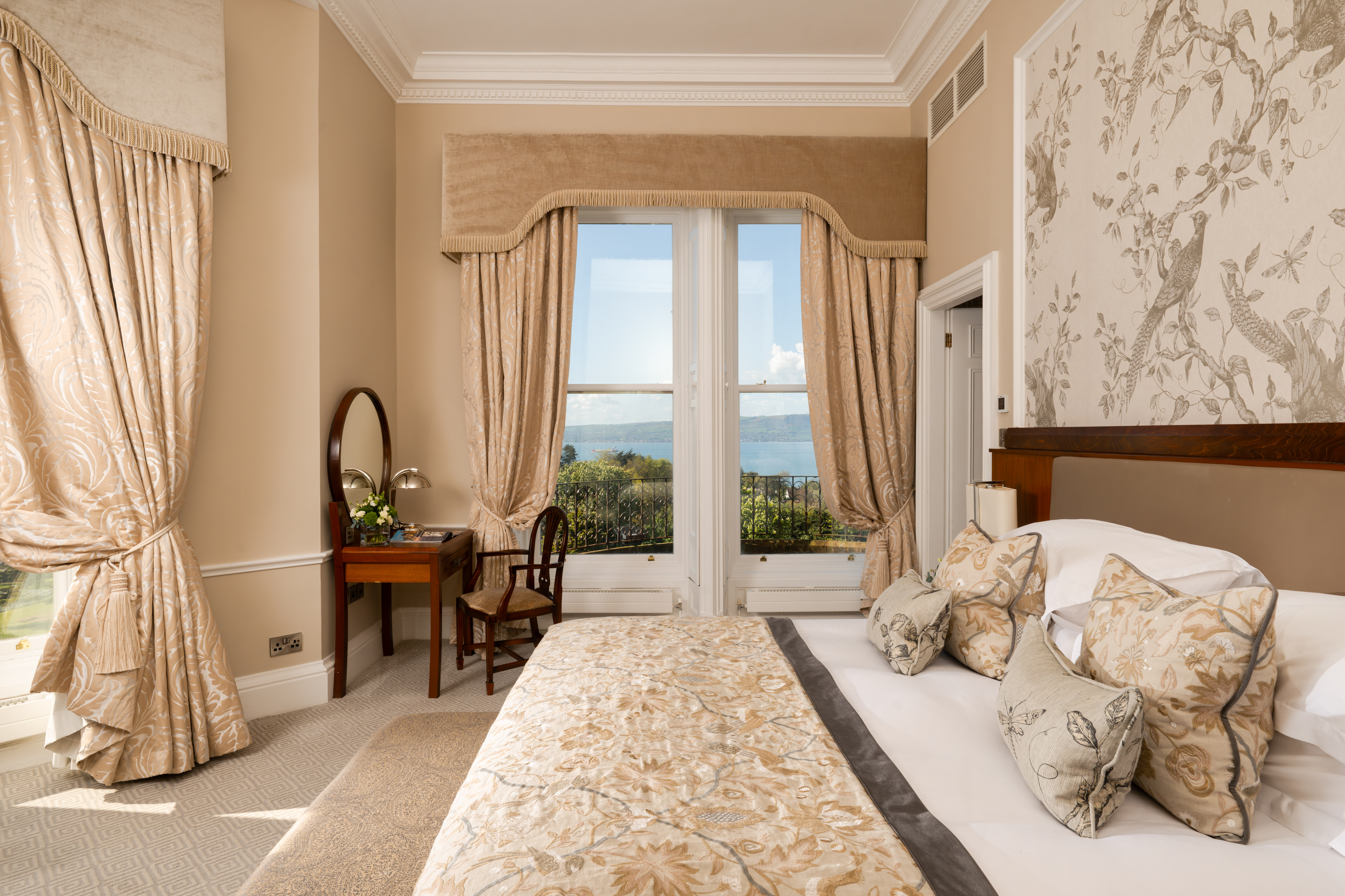Elegant bedroom with floral decor, large window view, and classic furniture.