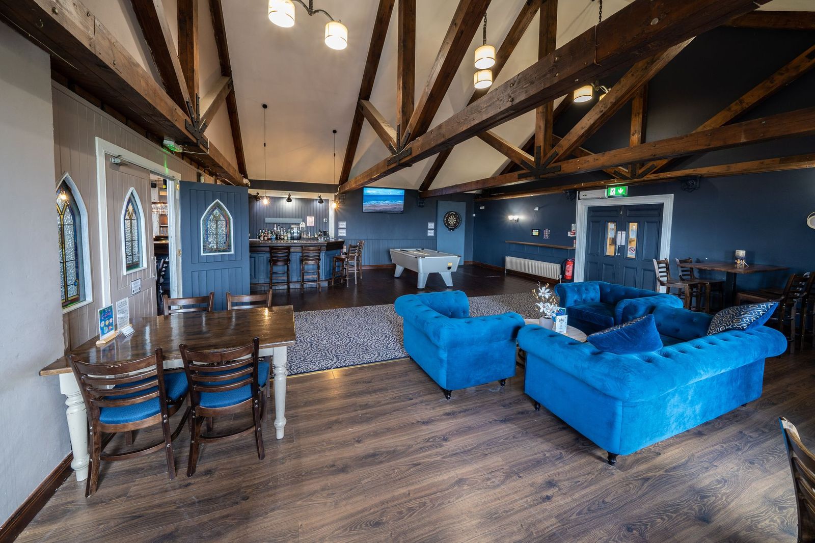 The spacious interior of a pub or clubhouse with blue sofas, a pool table, and a bar.