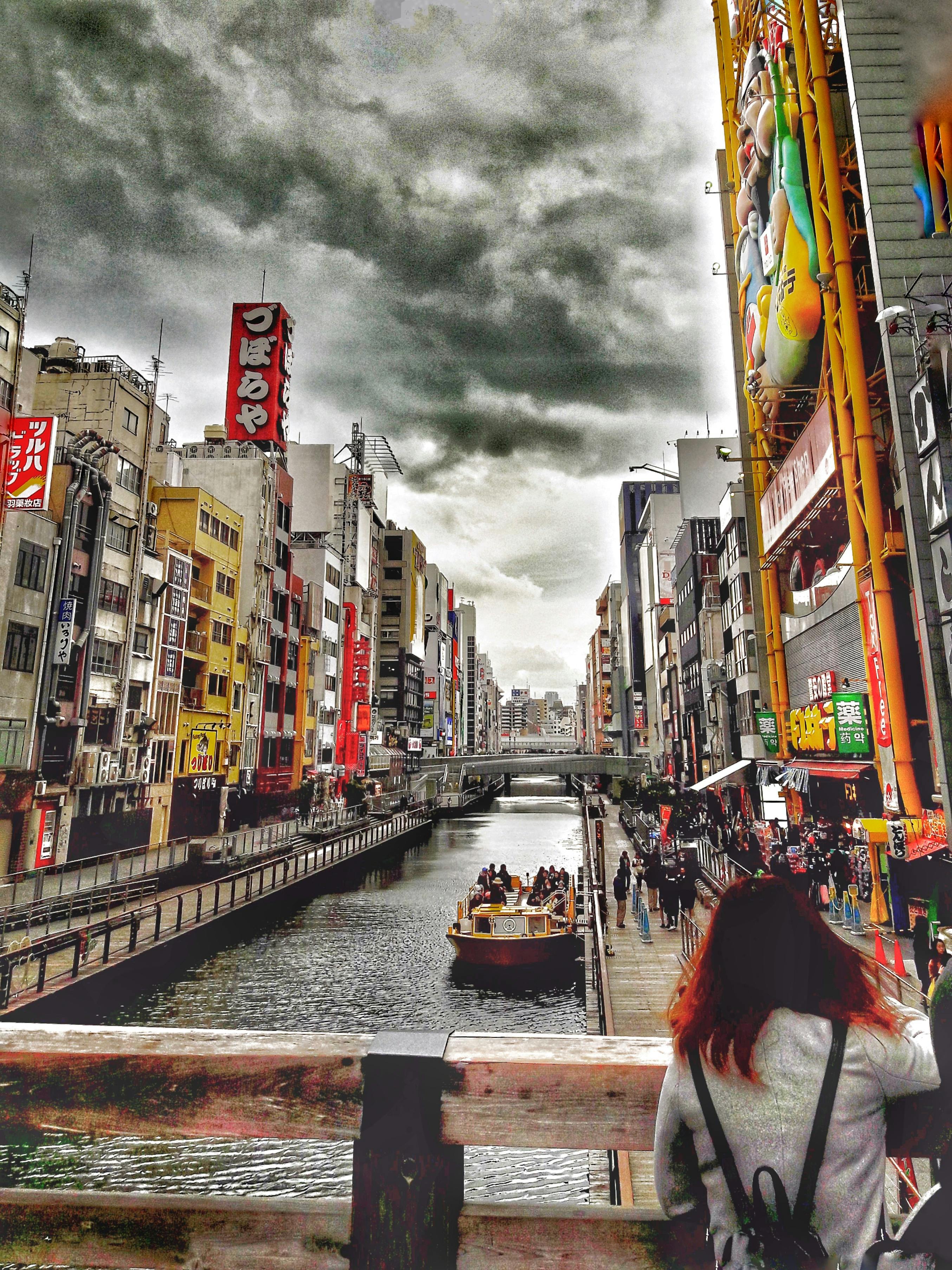 Urban canal scene with boat, colorful buildings, and cloudy sky.