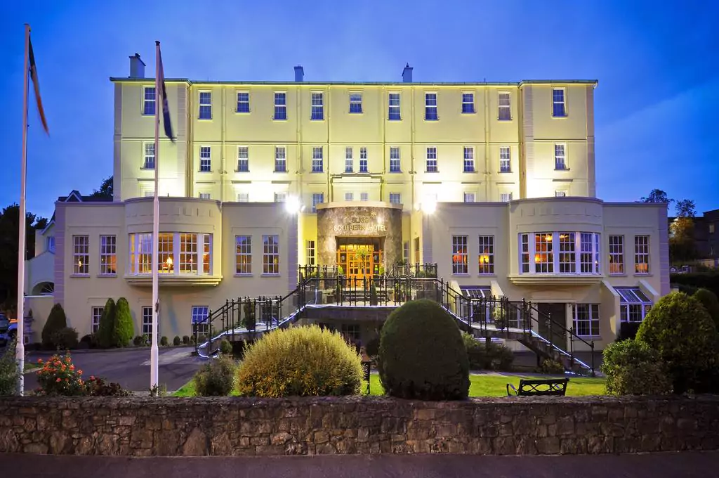 The exterior of the Sligo Southern Hotel, a large yellow building, illuminated at dusk with gardens in front.