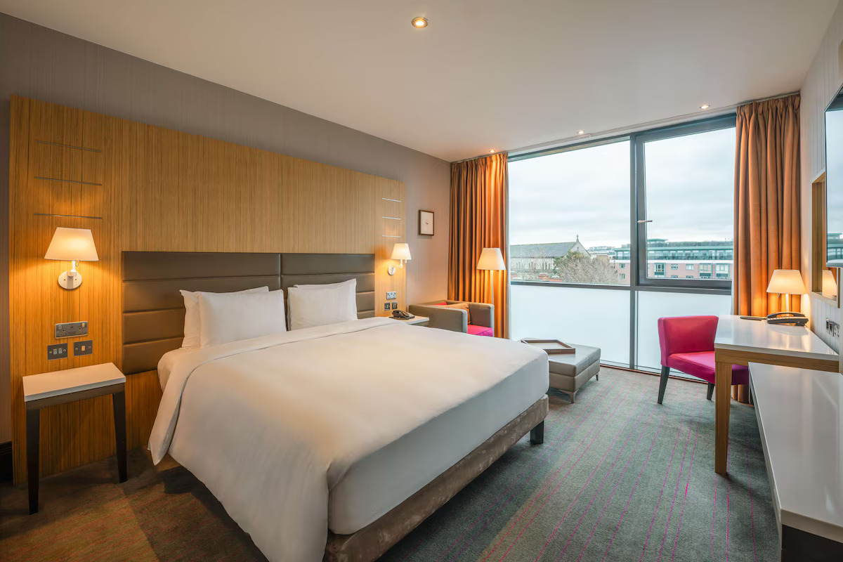 Modern hotel room with a large bed, lamps, and a window view.