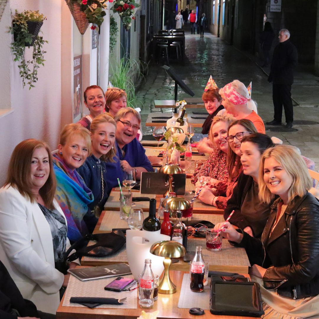 Group of people smiling and dining at a long outdoor table.