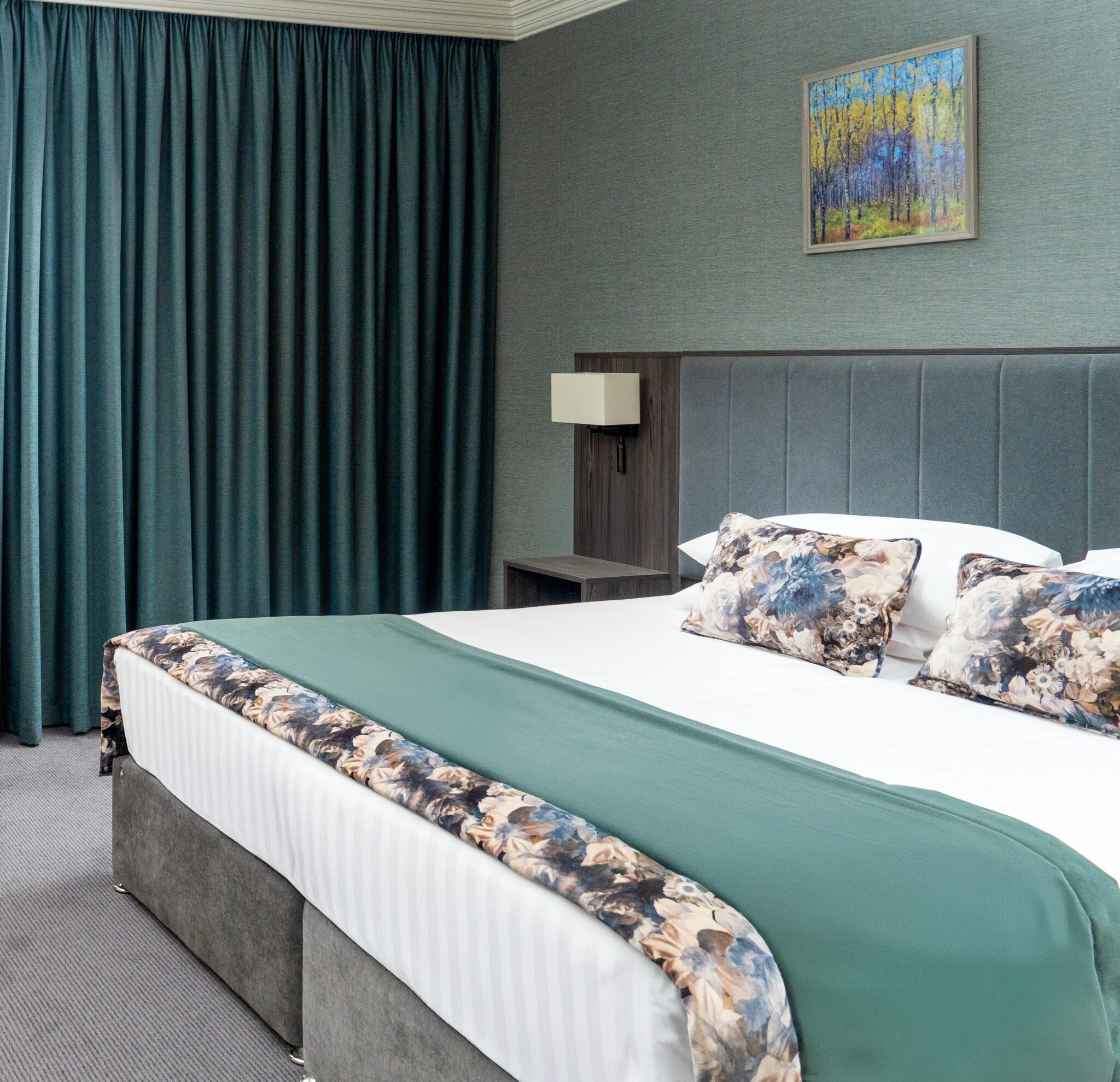 Hotel room with a double bed, floral pillows, and a landscape painting on the wall.