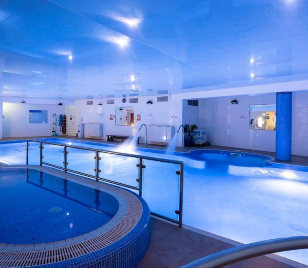 Indoor swimming pool with blue lighting and water jets.