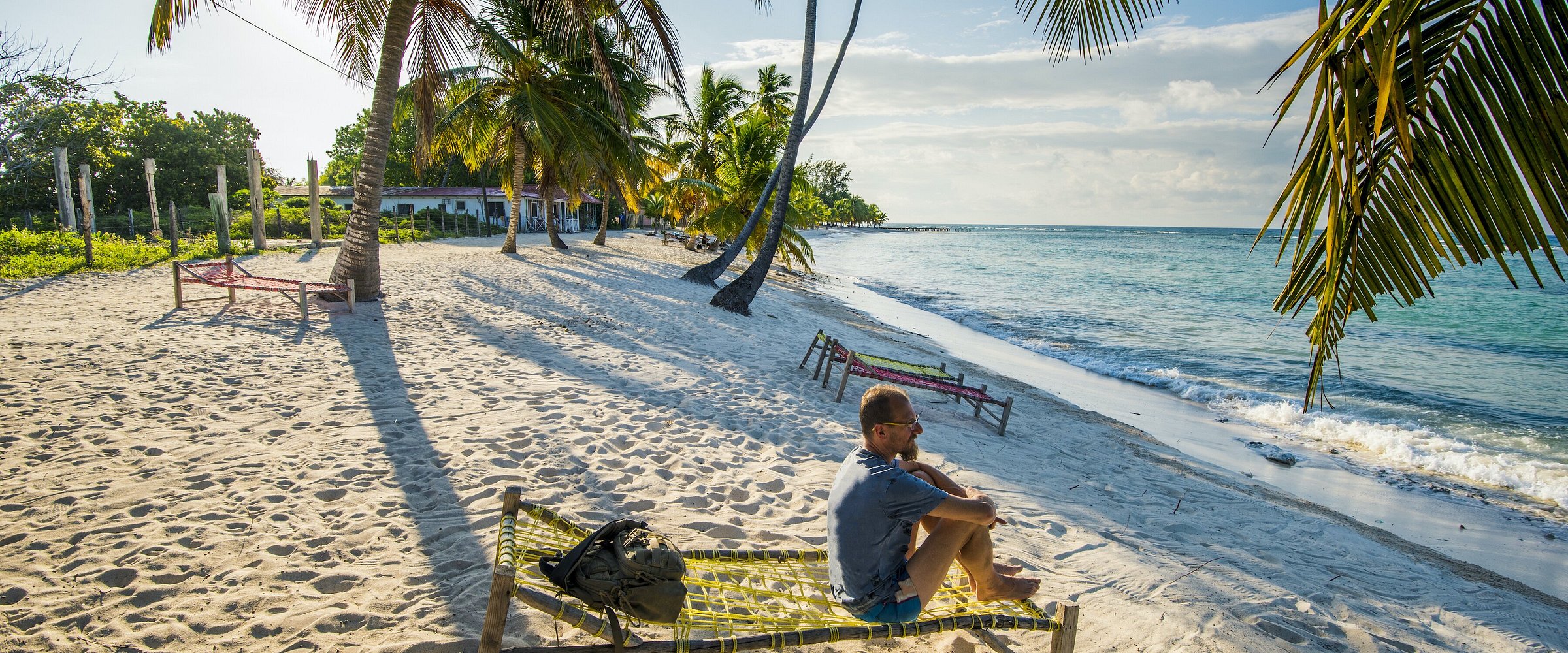 Person sitting on a hammock on a tropical beach with palm trees.