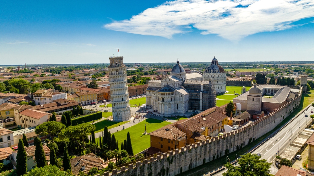 An aerial view of the Leaning Tower of Pisa and the surrounding cathedral complex on a sunny day.