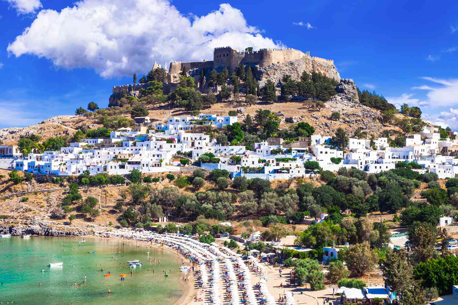 White buildings on a hillside with a beach and clear blue water.