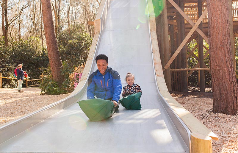 Two people sliding down a large outdoor slide with green mats.