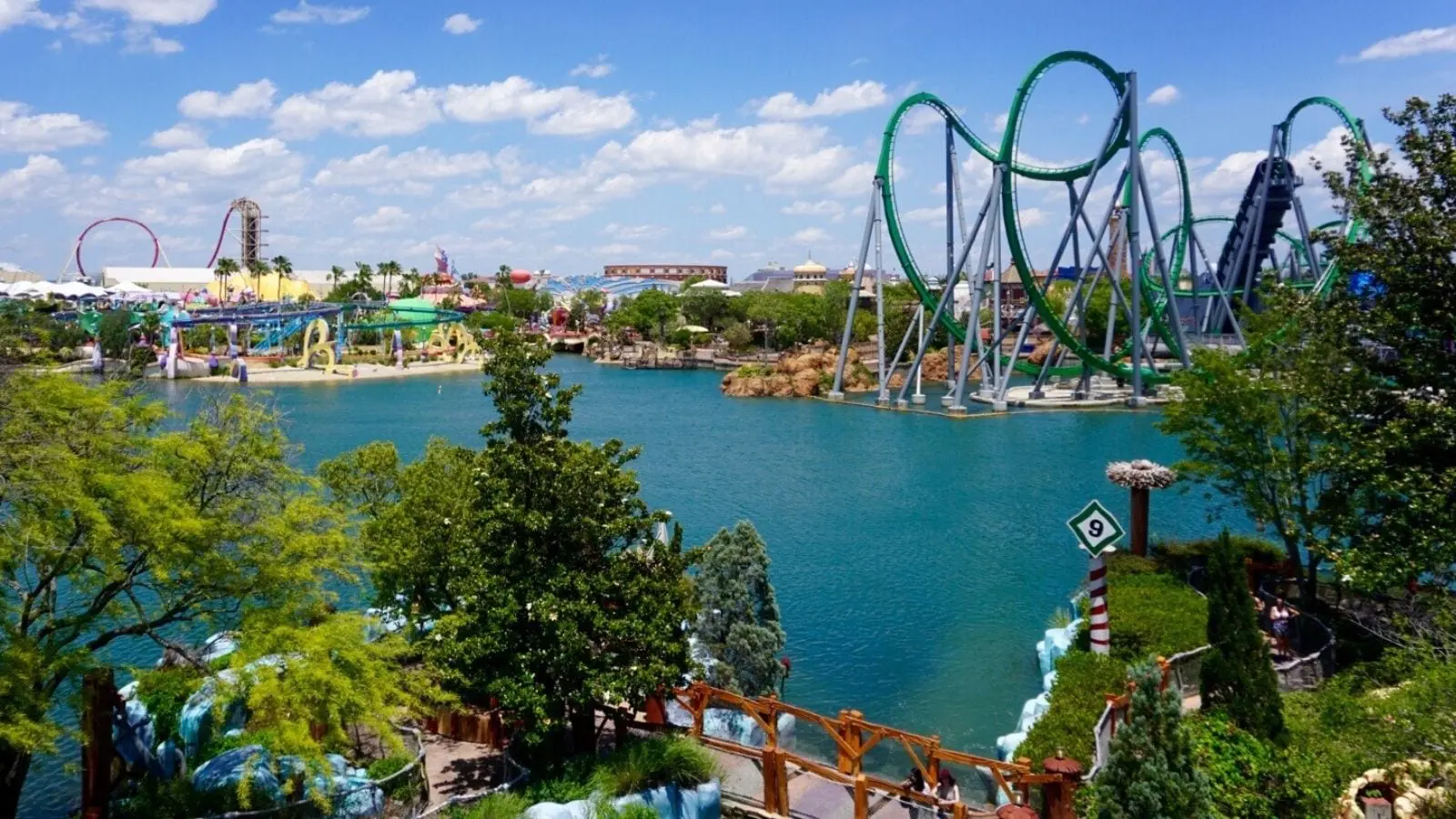 Amusement park with roller coasters and a lake under a blue sky.
