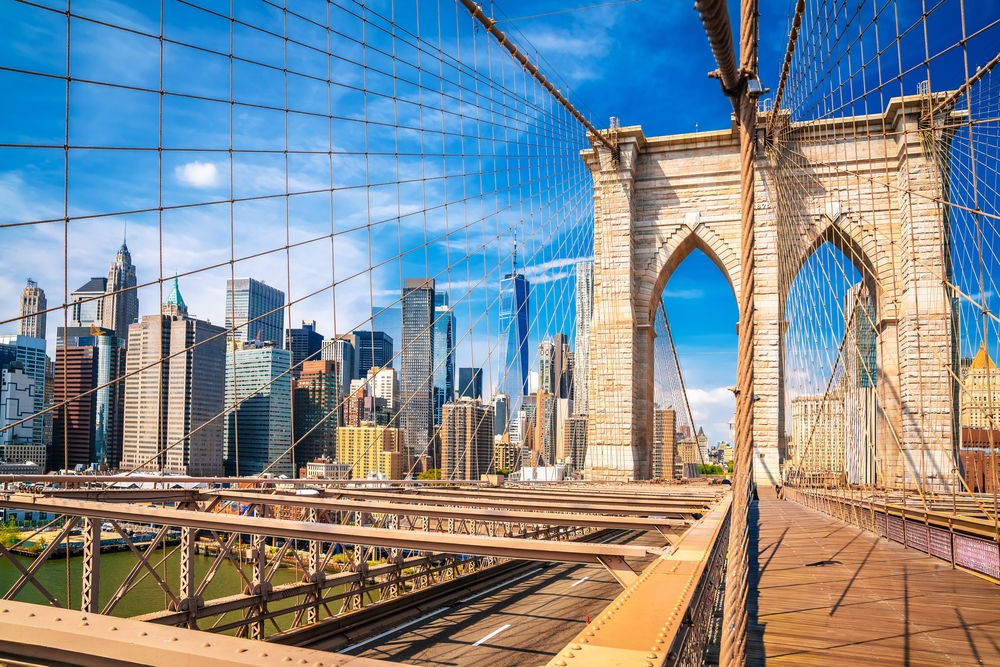 A sunny daytime view from the Brooklyn Bridge, looking towards the Manhattan skyline and skyscrapers.