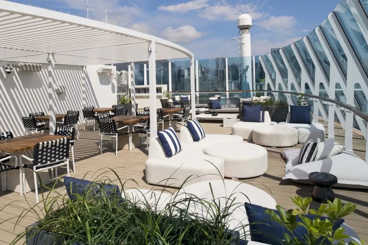 An outdoor lounge and dining area on a sunny rooftop deck with city views.
