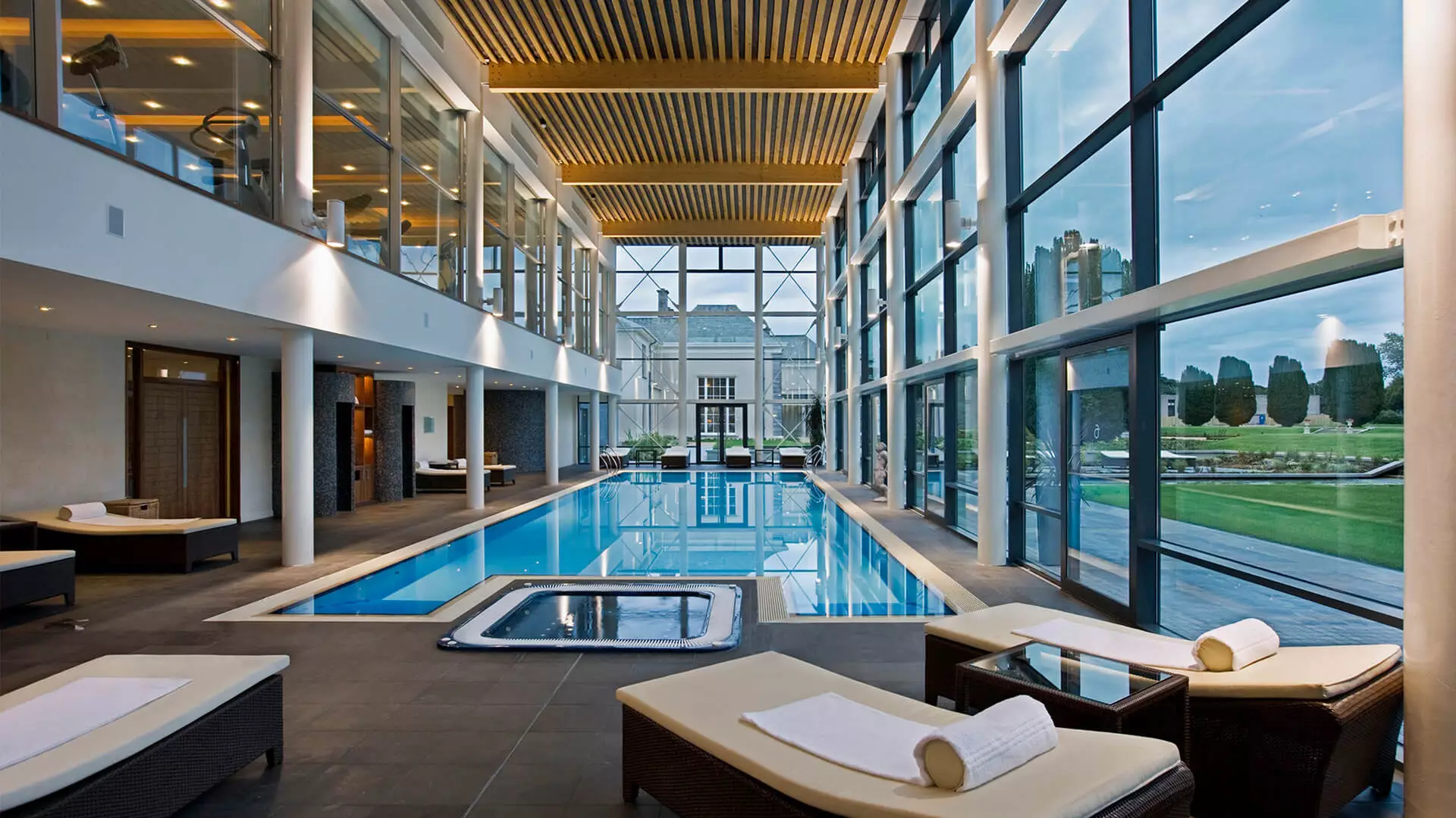 Luxurious indoor pool with lounge chairs and large windows overlooking a garden.