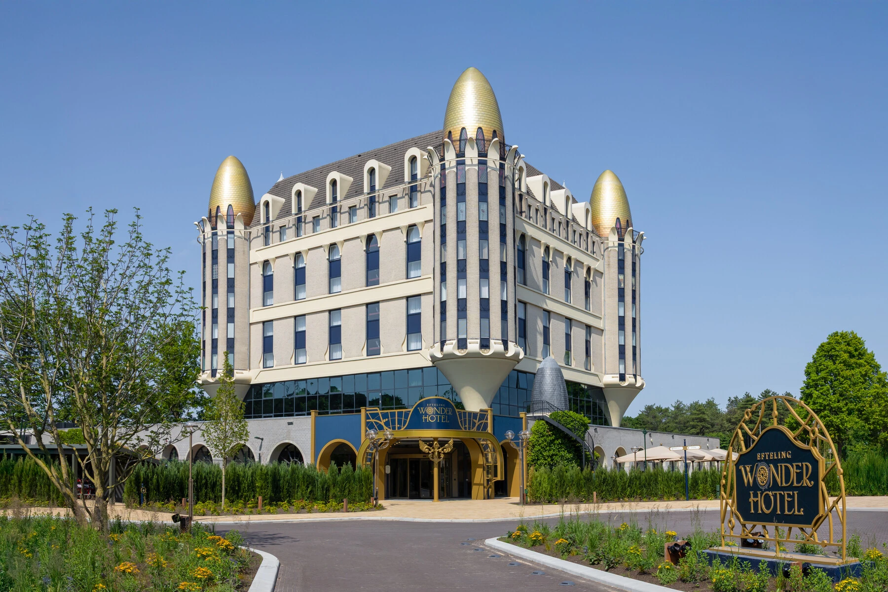 The Efteling Wonder Hotel, a whimsical castle-like building with golden domes, seen from its driveway on a sunny day.