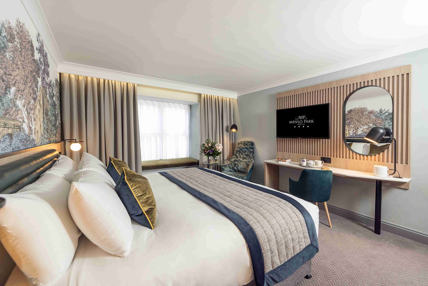 Modern hotel room with a bed, desk, chair, and wall-mounted TV.