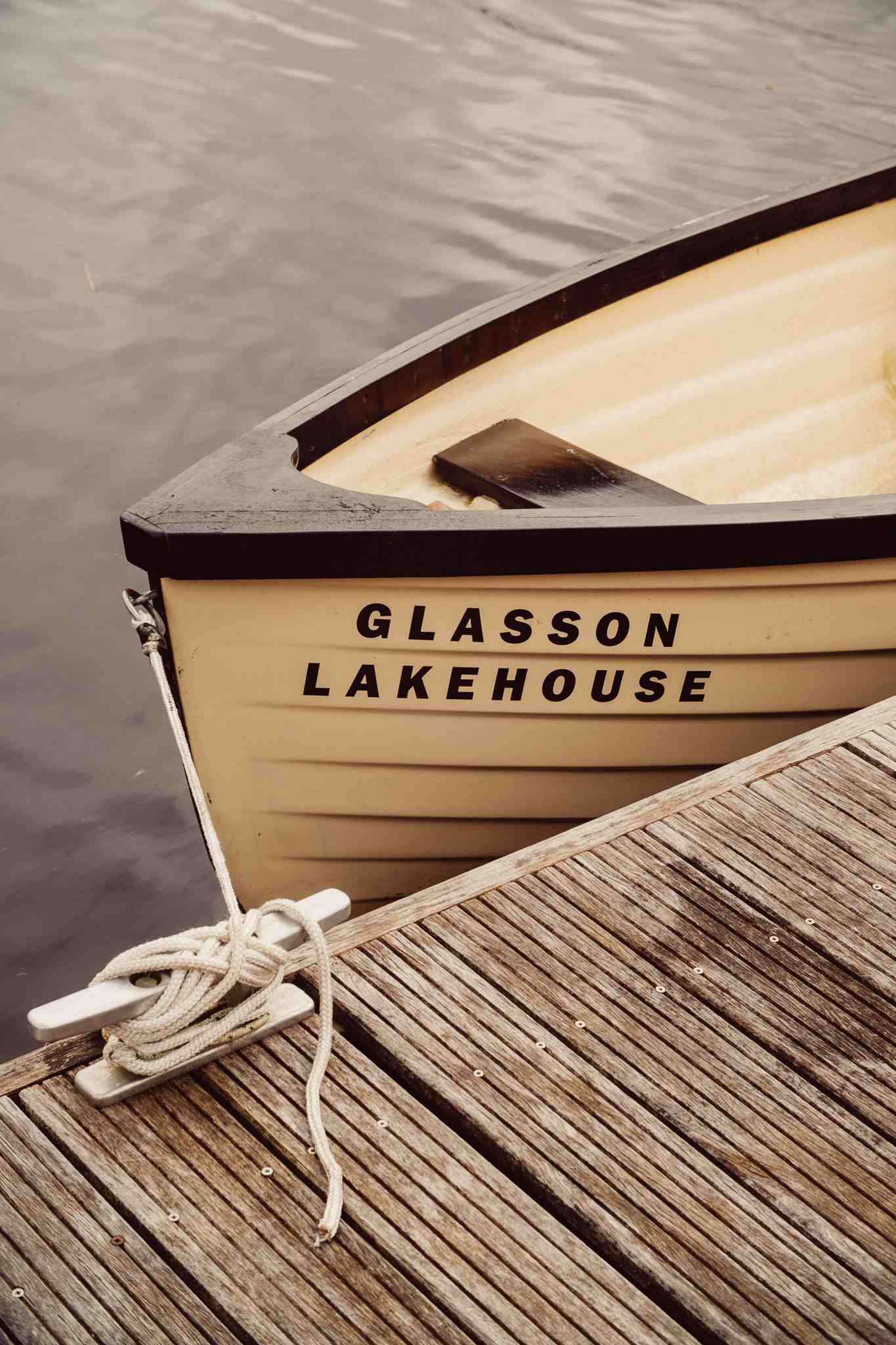 The bow of a cream-colored boat named 'Glasson Lakehouse' is tied to a wooden dock.