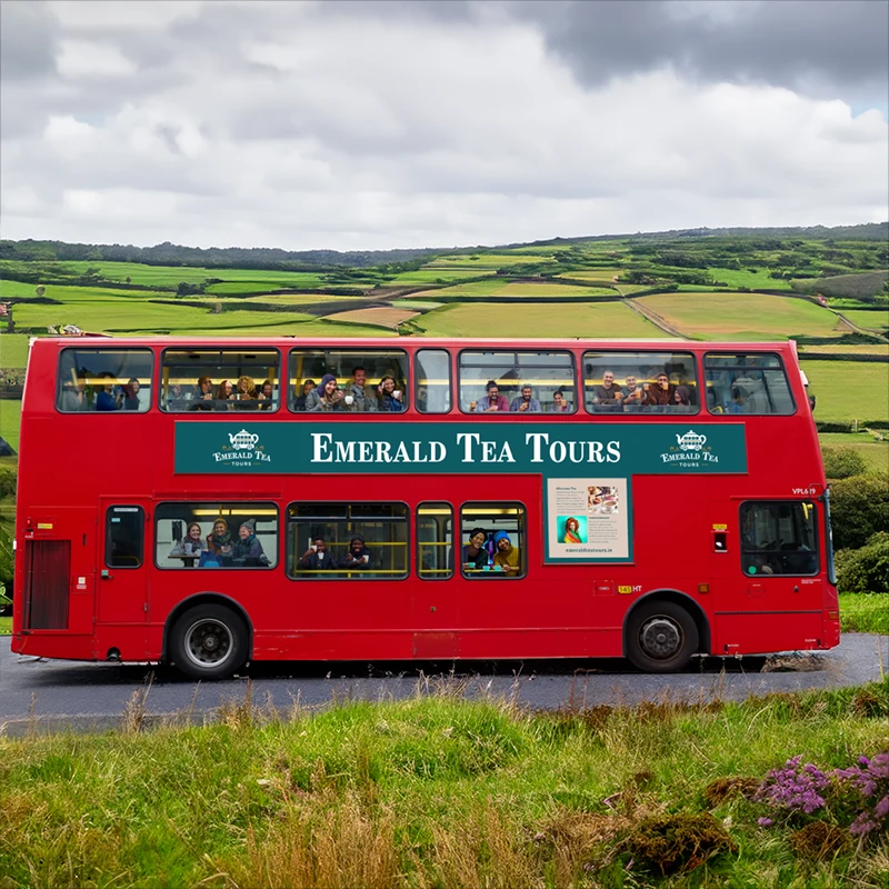 Red double-decker bus labeled 'Emerald Tea Tours' in a countryside setting.