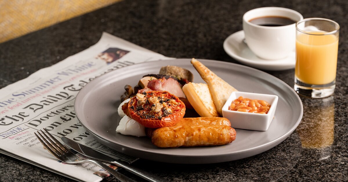 Full English breakfast with coffee, orange juice, and newspaper on a table.