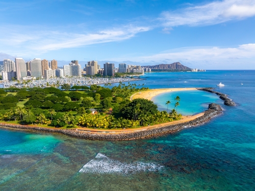 Aerial view of a tropical city skyline next to a park and a curved beach with a lagoon.