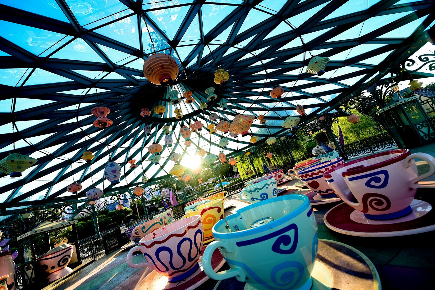Colorful teacup ride under a glass canopy with hanging lanterns.