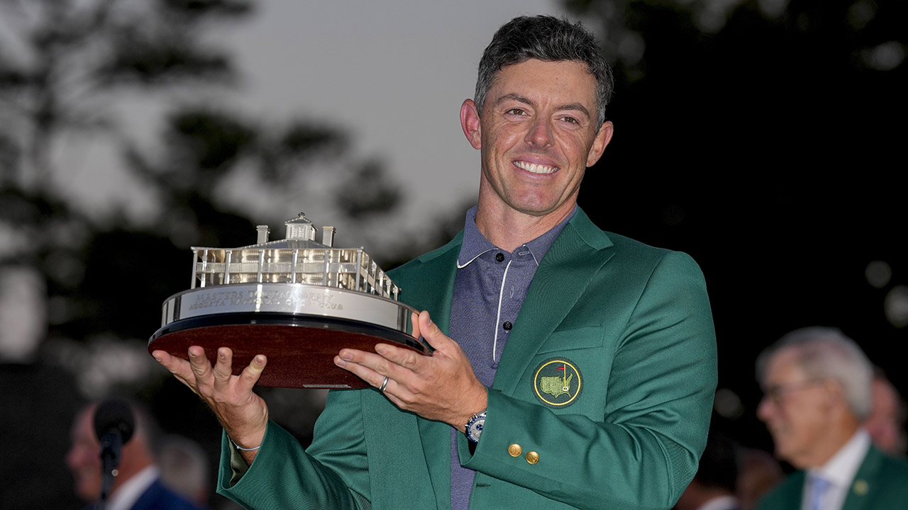 Person in green jacket holding a trophy with a building model.