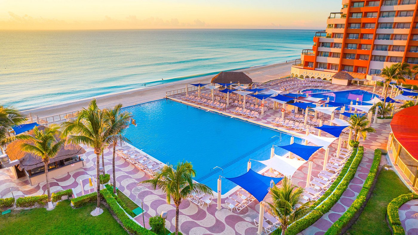 Beachfront resort with pool, palm trees, and ocean view at sunset.
