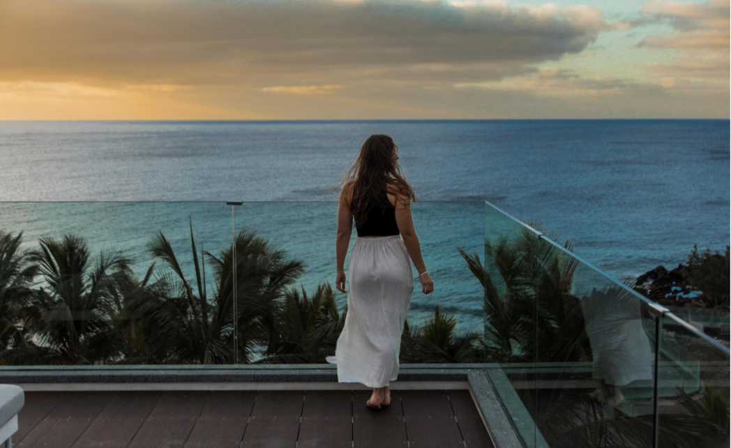 Woman in white skirt overlooking ocean at sunset.