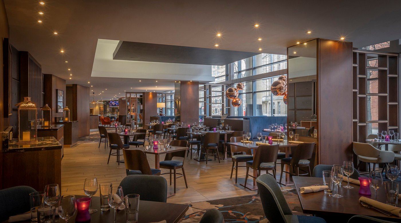 Modern restaurant interior with wooden tables, chairs, and decorative lighting.