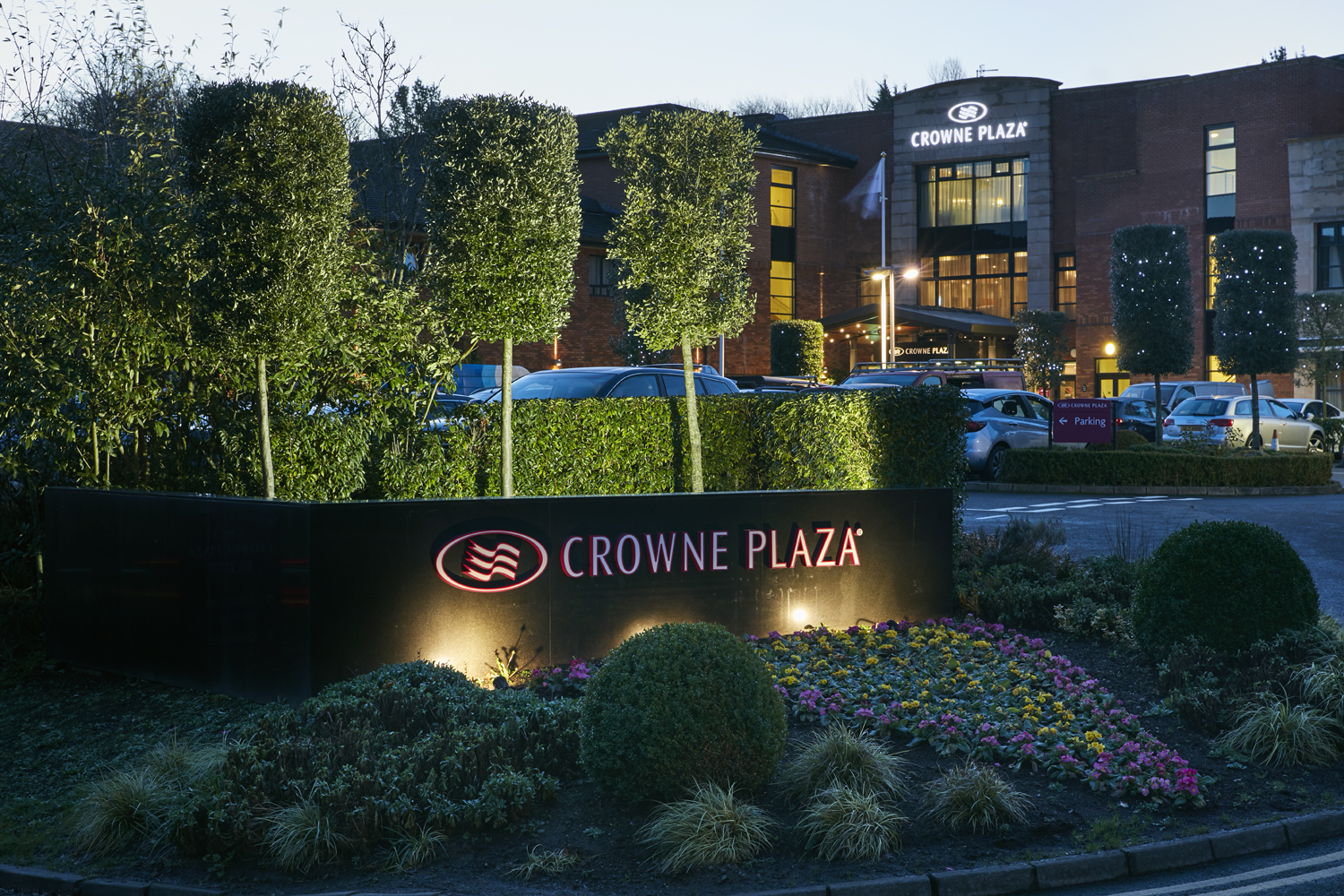 Night view of a Crowne Plaza hotel entrance with lit signage and surrounding greenery.