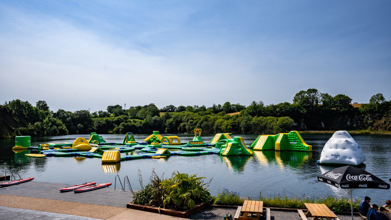Floating inflatable obstacle course on a lake with surrounding greenery.