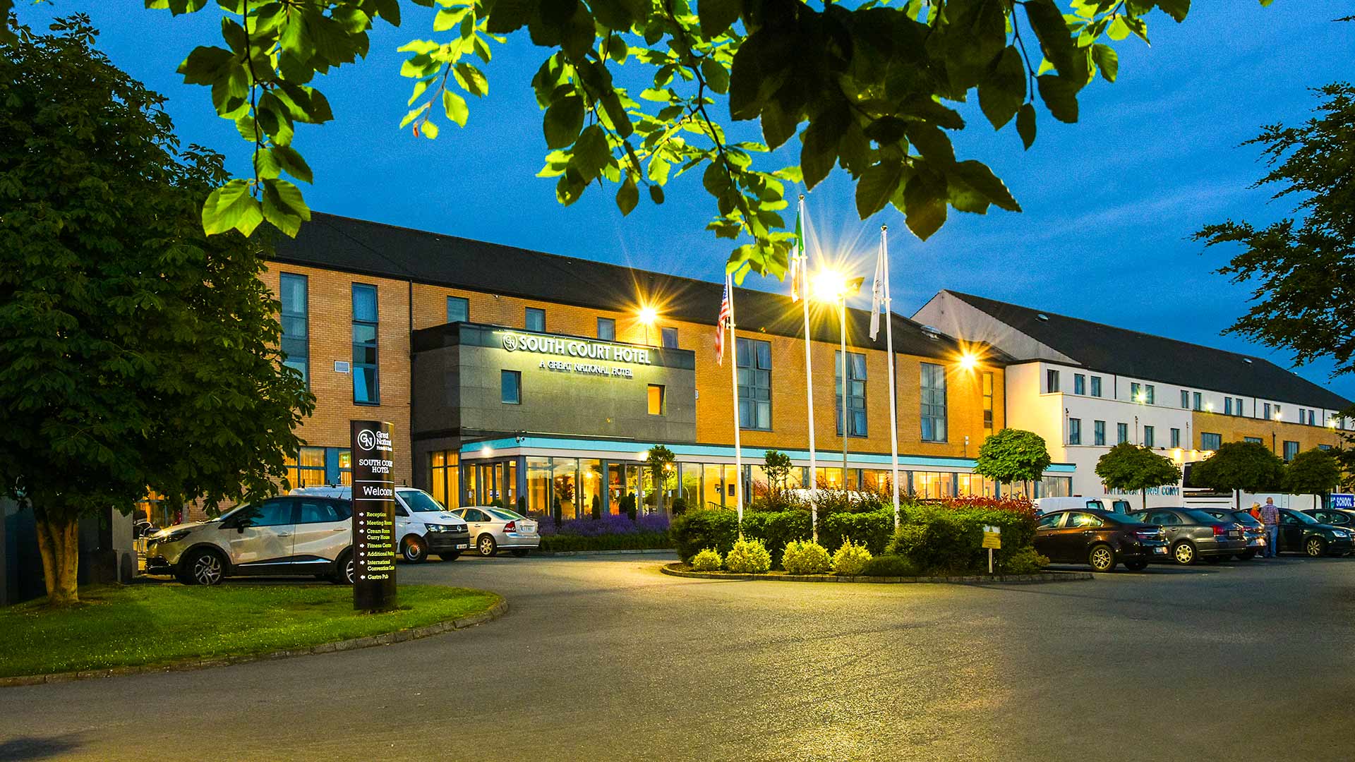 The exterior of the South Court Hotel at dusk, with lights on and cars in the parking lot.